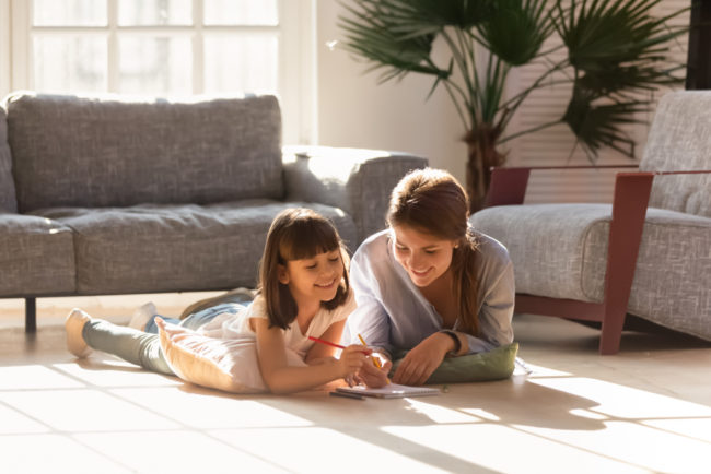 happy mum and daughter lying on a heated floor reading together