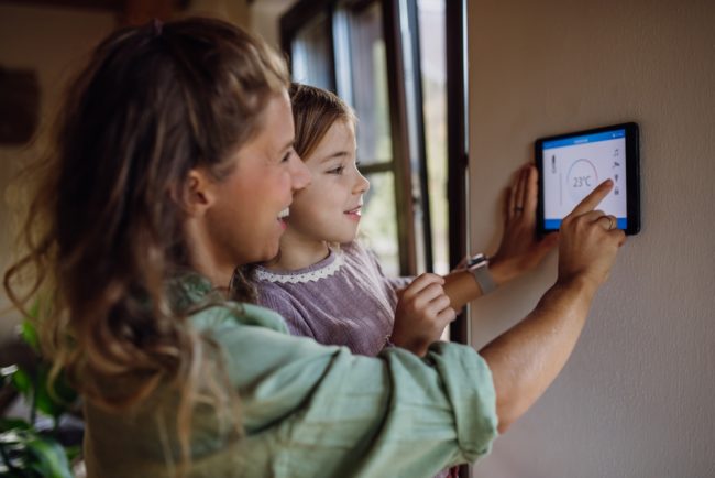 Girl,Helping,Mother,To,Adjust,,Lower,Heating,Temperature,On,Thermostat.